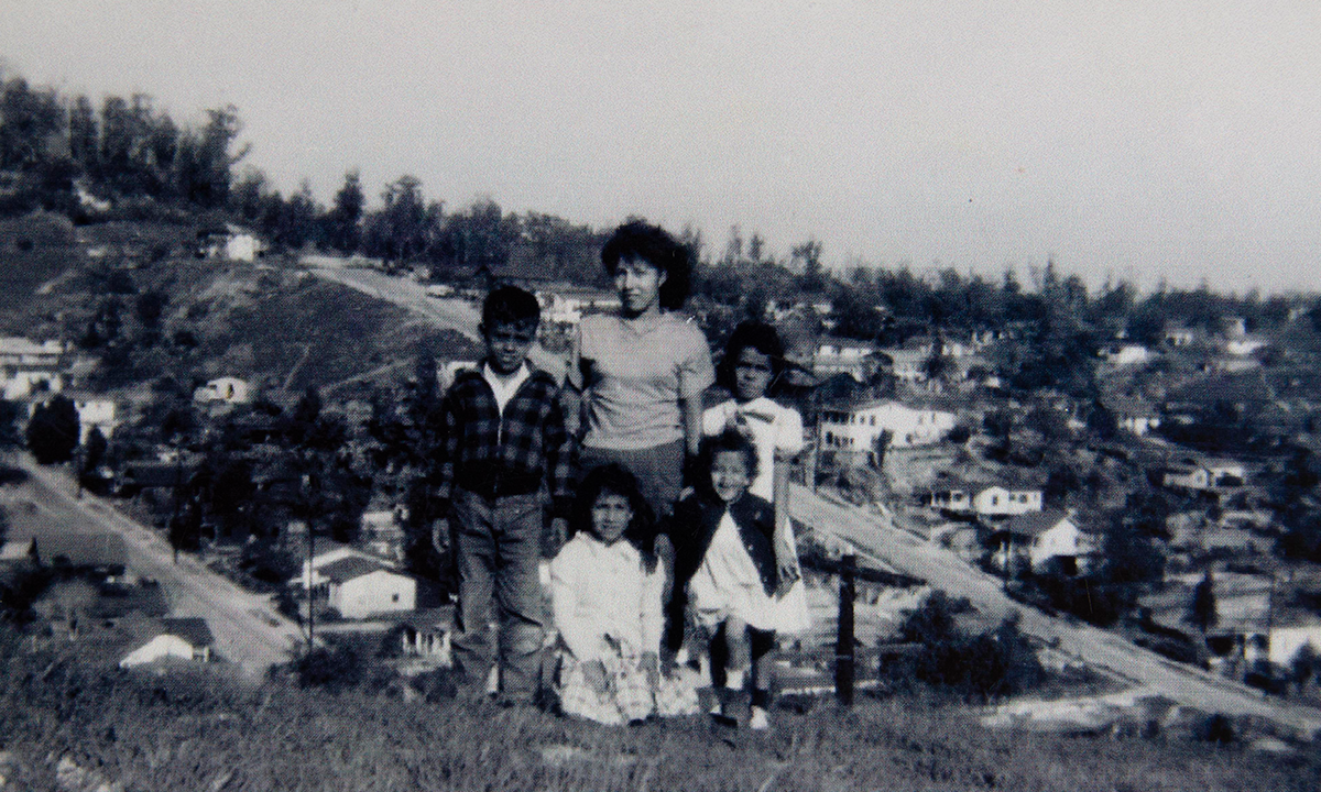 Black and white photo of one adult and 4 children standing on a ridge above a neighborhood.